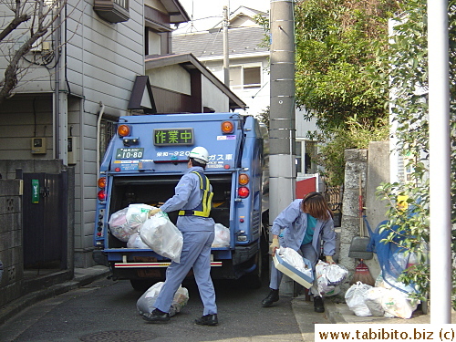 Garbage workers hard at work, the one on the right is a bit sloppy with his uniform