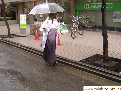 Talking on the cell phone while walking in heels dressed in constrictive clothing and balancing the umbrella from rain, this woman does the job well