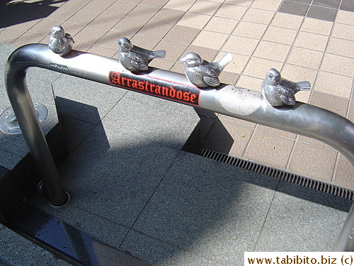 A row of metal birds adorns this rail in Shimokitazawa, someone also slapped a sticker on it