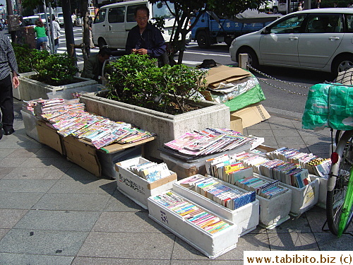 All kinds and sizes of used comic books for sale on the street. People who salvage comics from garbage bins and recycle boxes sell them to hawkers who in turn sell them for 100 yen each to the public