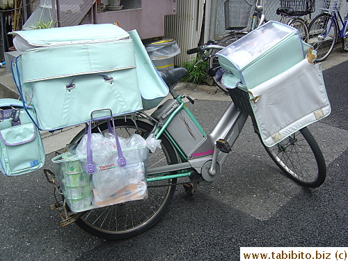 A Yakult Lady's bike. She has gone inside a building to make delivery leaving the bike on the street