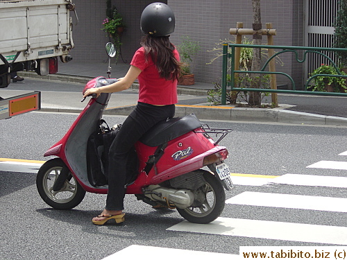 This woman wears wooden flip-flop style sandals to ride the motorbike. Hmmm?