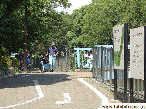 The cycle path rejoins the walkway beside the stream.  A baseball coach and his kid players take a run on the walkway