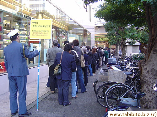 People line up to buy loto tickets. The sign this man's holding says: This is the end of the line to Window #1