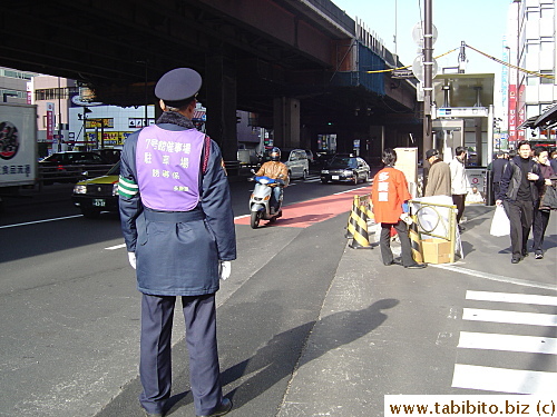 This guard with the purplr bib directs cars to the parking garage and number 7 building