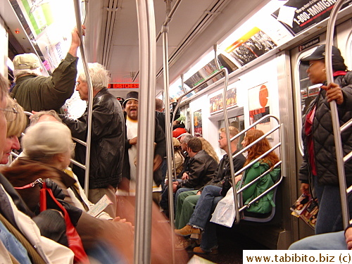 A spankingly new train in use in a line frequented by tourists.  The man coming down the aisle was performing for money