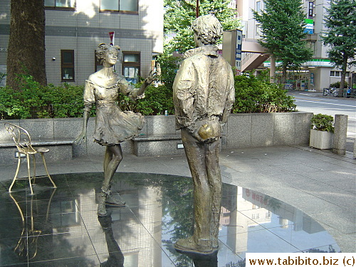 The man holds an apple behind him and the woman is ready to grab it