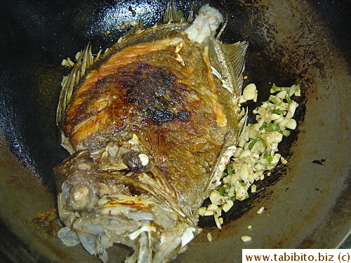 The fish is returned to the wok, tossed with the garlic, and splashed with cooking wine and spiced salt