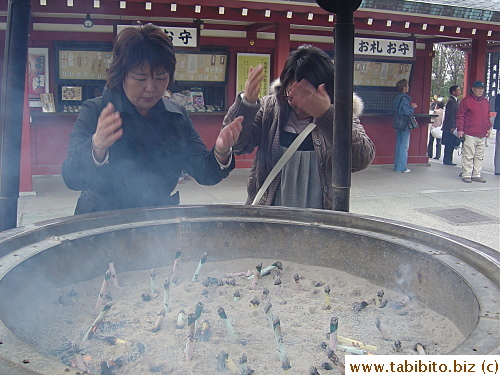 People fan smoke from burning incense to cleanse their body and soul